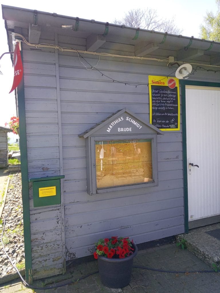 Graues Holzhaus mit Blumenkübel und Infotafel