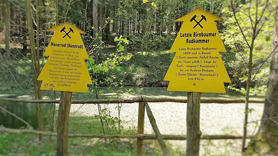 Yellow signs in the forest provide information about the water wheel and wheel chamber