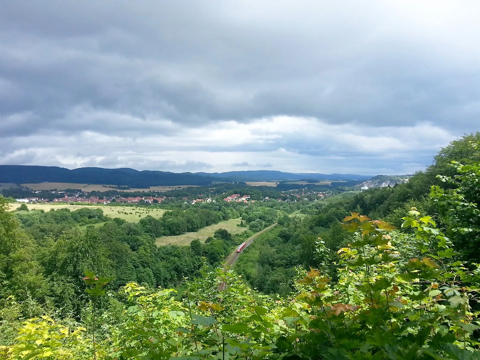 Landschaft mit Tal, Wäldern und Dorf unter Wolkenhimmel