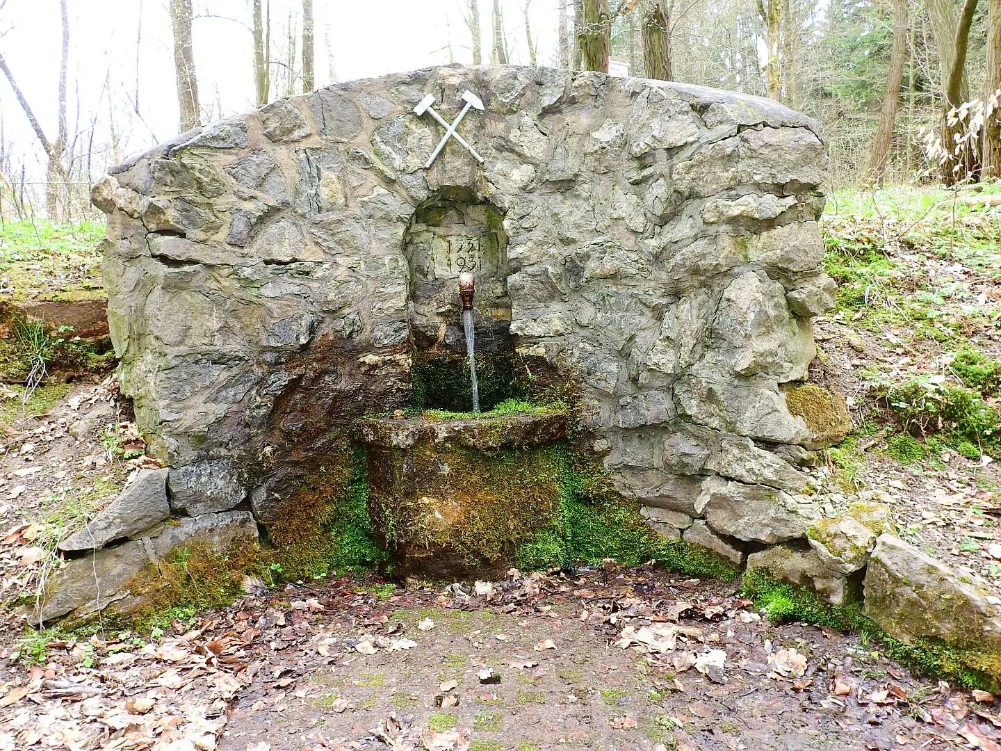 Old stone fountain in the forest with running water