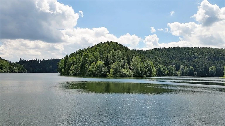 Ruhiger See mit bewaldeten Hügeln und Wolkenhimmel