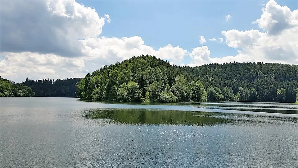 Ruhiger See mit bewaldeten Hügeln und Wolkenhimmel