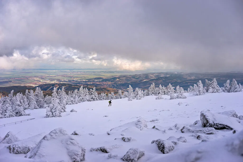 Verschneiter Brocken mit Wanderer. Winterlandschaft mit Blick ins Tal.