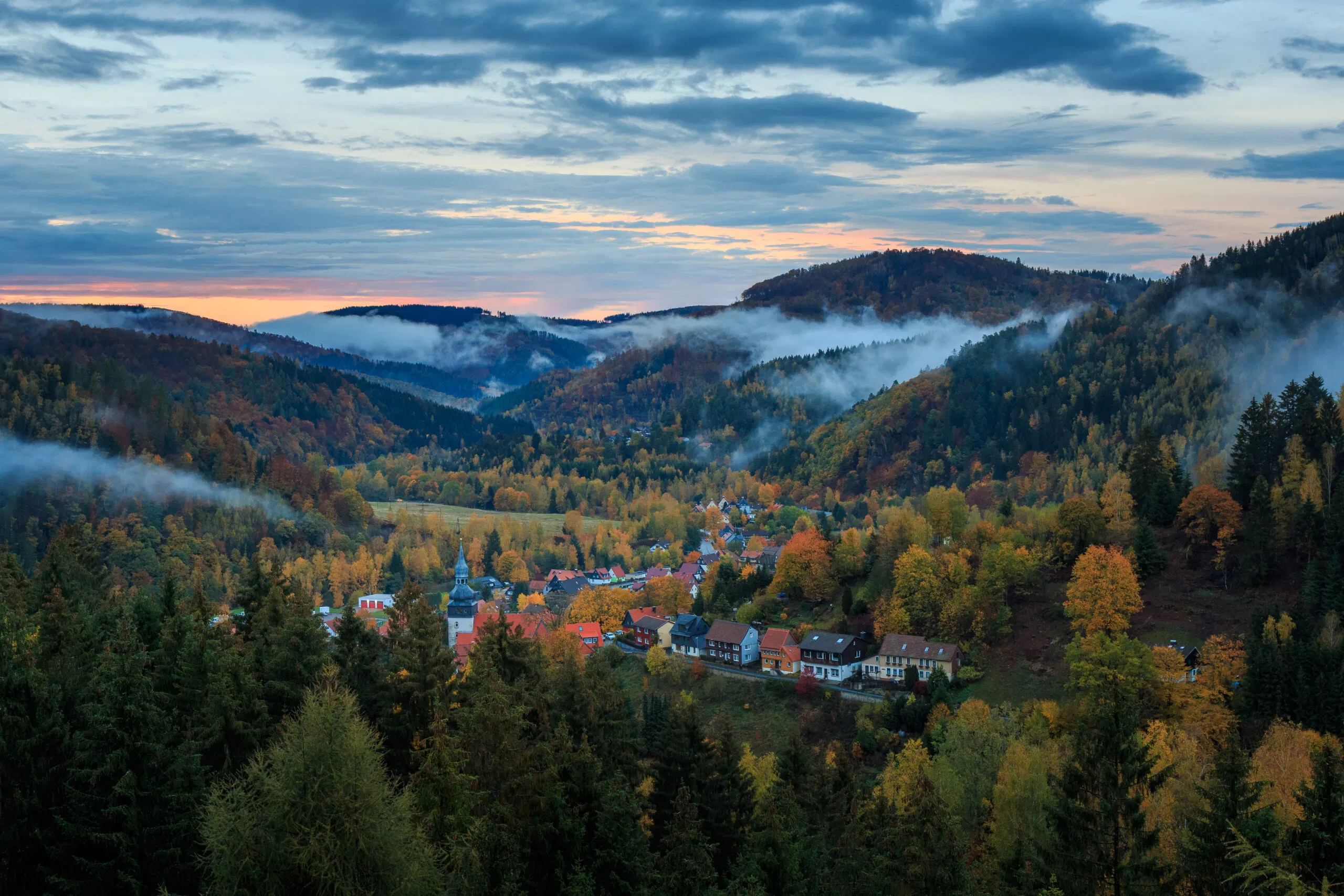 Herbstliches Dorf im Bergtal mit Morgennebel